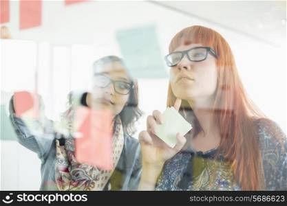Businesswomen reading sticky notes on glass wall in creative office