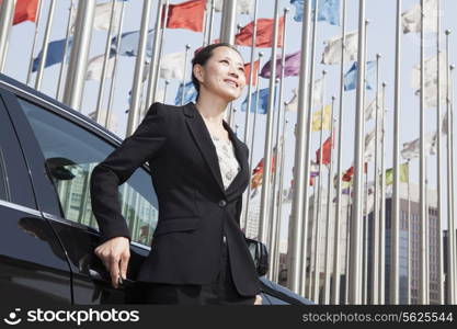 Businesswomen standing near car with flagpoles in background.
