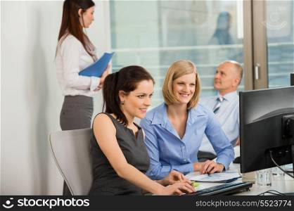 Businesswomen using computer with colleagues in background at office