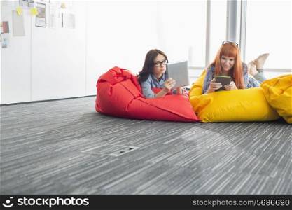 Businesswomen using digital tablets while relaxing on beanbag chairs in creative office