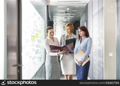 Businesswomen with file folders discussing in office corridor
