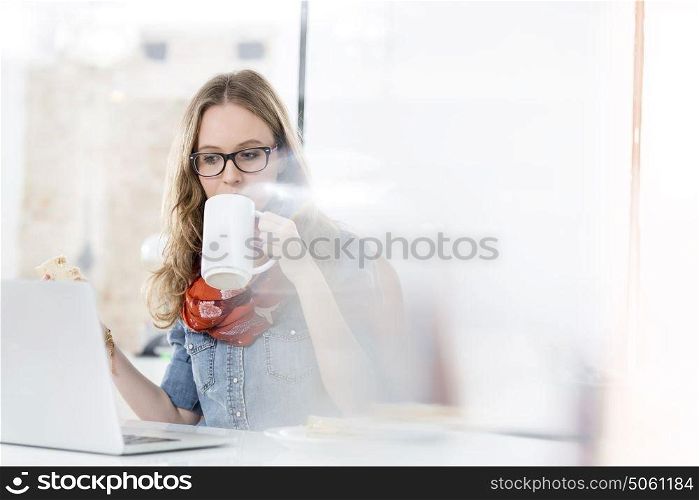Busy businesswoman having sandwich and coffee while working at desk
