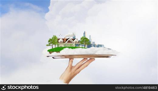 Busy city or countryside calm life. Hand holding metal tray with model of modern city and suburban house