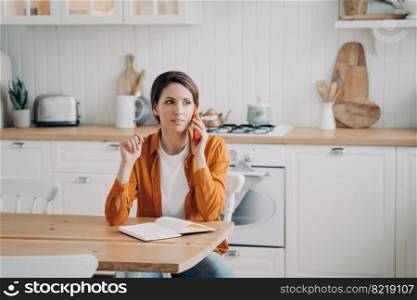 Busy female housewife talking on phone, calling to customer service, sitting in kitchen at home. Woman freelance worker discussing business issue, speaking on smartphone. Domestic life, remote job.. Female calling to customer service by phone, sitting in kitchen at home. Domestic life, remote job