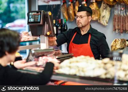 Butcher attending a customer in a butcher&rsquo;s shop weighing the meat and charging. Butcher attending a customer in a butcher&rsquo;s shop