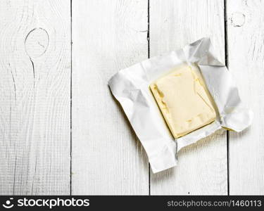 Butter on paper. On a white wooden background.. Butter on paper.