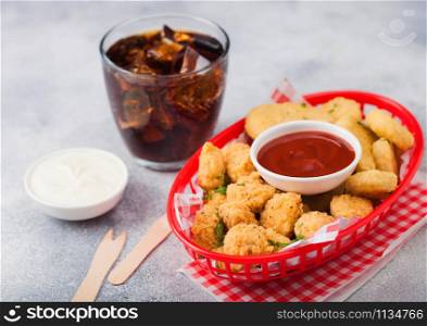 Buttered chicken nuggets and popcorn bites in red fast food basket with ketchup and glass of cola on light background with sour and cream sauce.