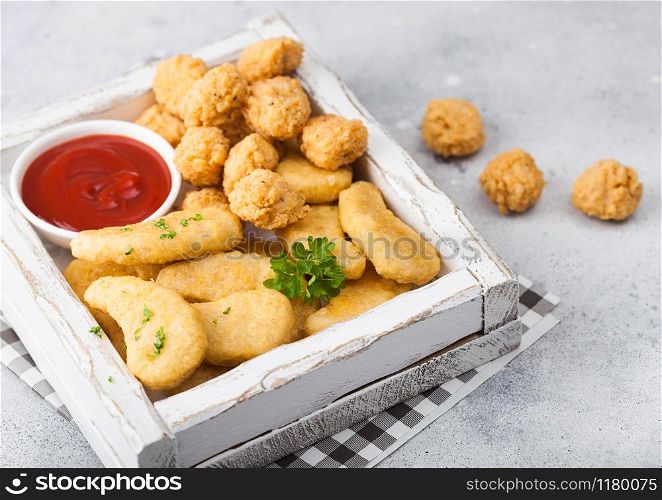 Buttered chicken nuggets and popcorn bites in white vintage wooden box with ketchup on light background. Fast food snack bar.