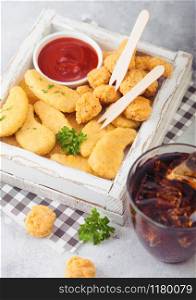 Buttered chicken nuggets and popcorn bites in white vintage wooden box with ketchup and glass of cola on light background. Fast food snack bar.