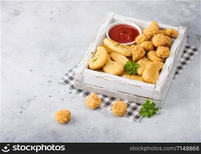 Buttered chicken nuggets and popcorn bites in white vintage wooden box with ketchup on light background. Fast food snack bar.