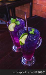 Butterfly pea juice with lemon in clear glass put on dark brown wooden table are thai herb drink for health and refreshing. Select focus