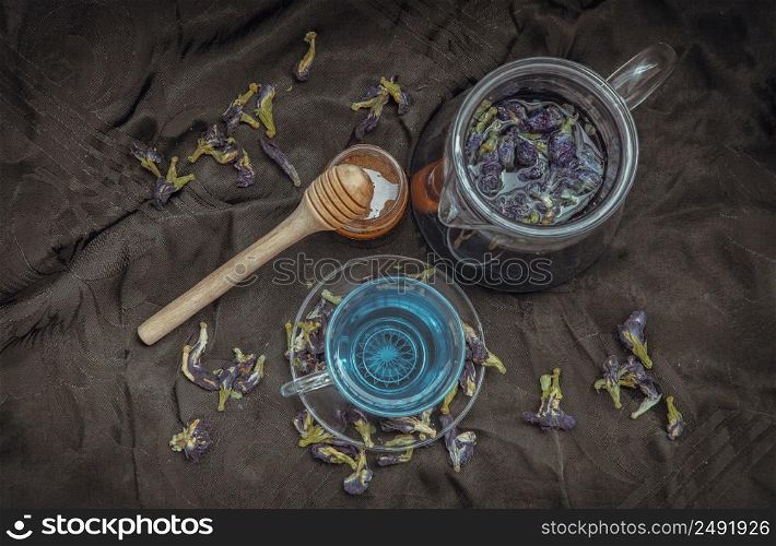 Butterfly pea tea (Clitoria) or Organic blue anchan in Teapot and glass cup served with honey on Dark background. Healthy detox herbal drink, Top view, Selective focus.
