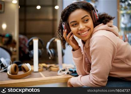 Buyer choosing headphones in audio store, music fan. Female person in music shop, showcase with earphones on background, woman in multimedia salon. Buyer choosing headphones in audio store