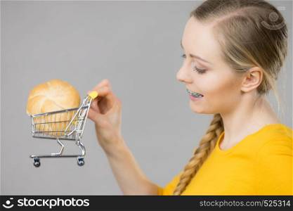 Buying gluten food products concept. Happy woman holding shopping cart trolley with bun breal roll. Woman holding shopping cart with bread