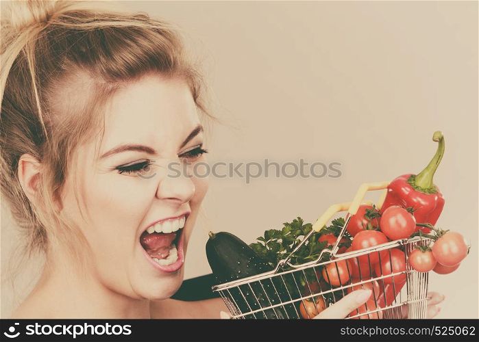 Buying good food, vegetarian products. Positive funny woman holding shopping basket with green red vegetables inside, recommending healthy high fibre diet, lifestyle modification, on grey. Woman holds shopping basket with vegetables