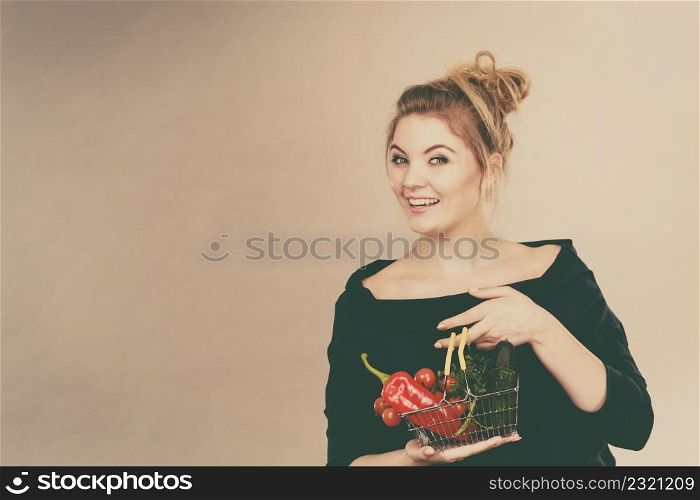 Buying good food, vegetarian products. Positive woman holding shopping basket with green red vegetables inside, recommending healthy high fibre diet, lifestyle modification, on grey. Woman holds shopping basket with vegetables