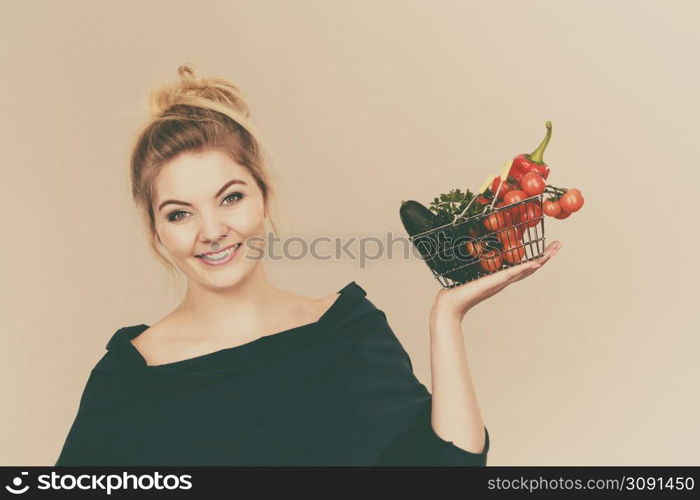 Buying good food, vegetarian products. Positive woman holding shopping basket with green red vegetables inside, recommending healthy high fibre diet, lifestyle modification, on grey. Woman holds shopping basket with vegetables