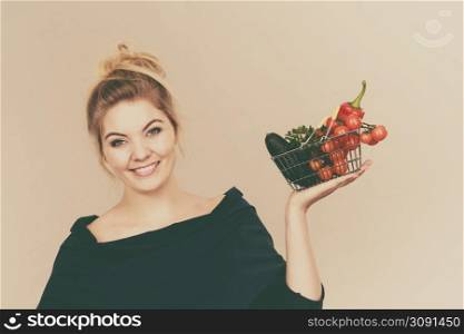 Buying good food, vegetarian products. Positive woman holding shopping basket with green red vegetables inside, recommending healthy high fibre diet, lifestyle modification, on grey. Woman holds shopping basket with vegetables