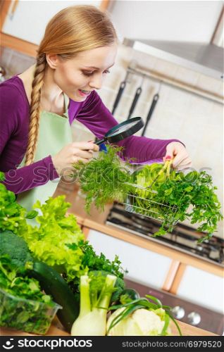 Buying healthy dieting food concept. Woman in kitchen having many green vegetables looking through magnifier at shopping basket trolley.. Woman looking through magnifier at vegetables basket