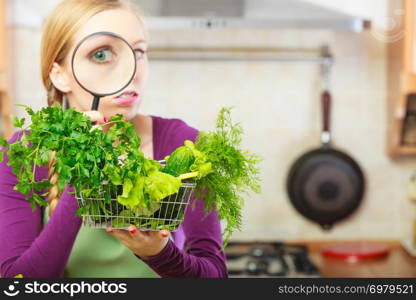 Buying healthy dieting food concept. Woman in kitchen having many green vegetables looking through magnifier at shopping basket trolley.. Woman looking through magnifier at vegetables basket