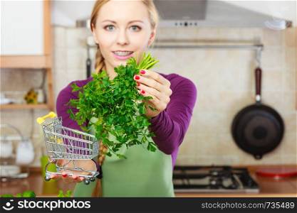 Buying healthy dieting food concept. Woman in kitchen having many green vegetables holding small shopping cart trolley with parsley inside.. Woman holding shopping cart with parsley inside