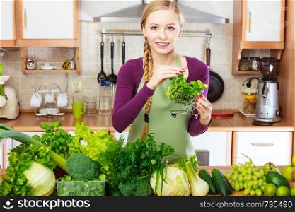 Buying healthy dieting food concept. Woman in kitchen having many green vegetables holding small shopping basket trolley.. Woman in kitchen having vegetables holding shopping basket