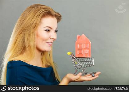 Buying property or home, real estate investment concept. Happy woman holding shopping cart with house inside. Woman holding shopping cart with house inside