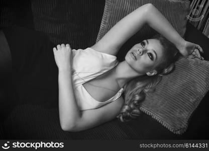 BW fashion shot of cute girl . she is laying on a sofa i her living room , has blond long hair , and looking up wth a dream expression