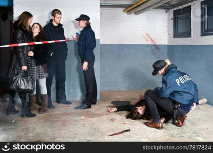 Bystanders being held at a distance by a police man at a murder scene, with a police woman tending to the victim