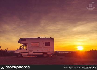 C&ing on nature beach. Caravan recreational vehicle at sunrise on mediterranean coast in Spain. Vacation and travelling in motorhome.. C&er car on beach at sunrise