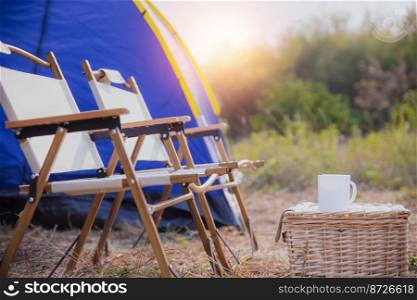 C&ing tent with coffee cup on desk and chairs in forest in morning