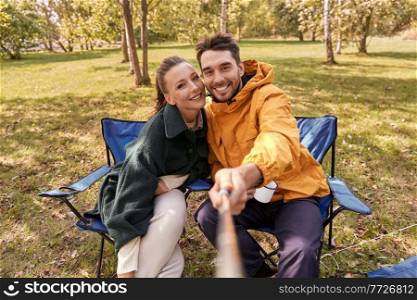 c&ing, tourism and travel concept - happy couple drinking tea and taking selfie at tent c&. couple drinking tea and taking selfie at tent c&