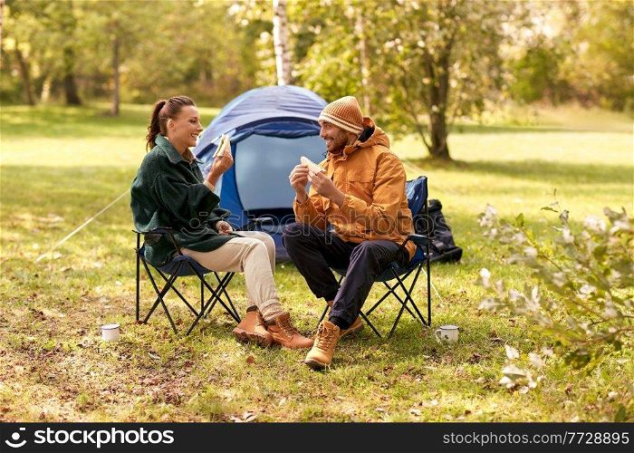 c&ing, tourism and travel concept - happy couple eating sandwiches at tent c&. happy couple eating sandwiches at tent c&