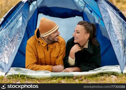 c&ing, tourism and travel concept - happy couple lying inside tent at c&site. happy couple lying inside tent at c&site