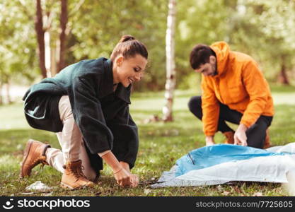 c&ing, tourism and travel concept - happy couple setting up tent outdoors. happy couple setting up tent outdoors