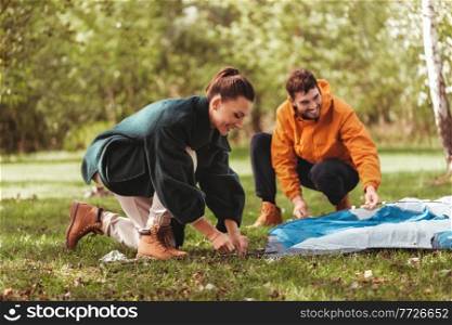 c&ing, tourism and travel concept - happy couple setting up tent outdoors. happy couple setting up tent outdoors
