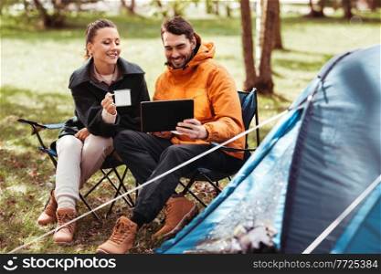 c&ing, tourism and travel concept - happy couple with tablet pc computer drinking tea at tent c&. couple with tablet pc drinking tea at tent c&