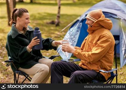 c&ing, tourism and travel concept - happy couple with thermos drinking tea to cup at tent c&. couple with thermos drinking tea at tent c&