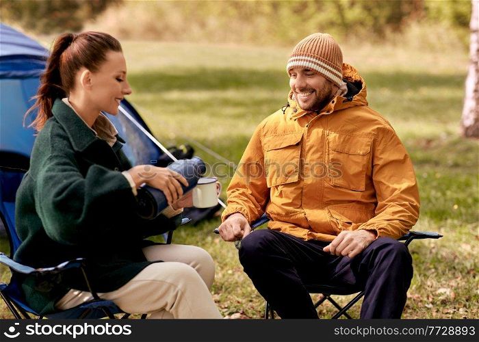 c&ing, tourism and travel concept - happy couple with thermos pouring tea to cup at tent c&. happy couple with thermos pouring tea at tent c&