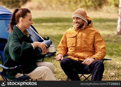 c&ing, tourism and travel concept - happy couple with thermos pouring tea to cup at tent c&. happy couple with thermos pouring tea at tent c&