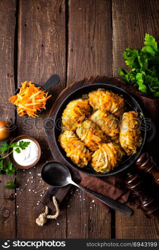 Cabbage rolls stewed with meat and vegetables in pan on dark wooden background, top view