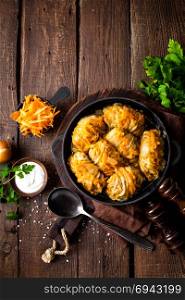 Cabbage rolls stewed with meat and vegetables in pan on dark wooden background, top view
