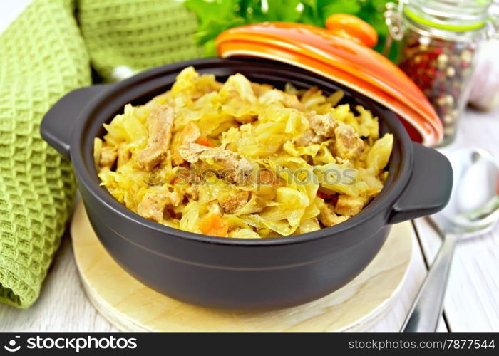 Cabbage stew with meat in black roasting pan with lid, green napkin, pepper, parsley, spoon on a light background boards