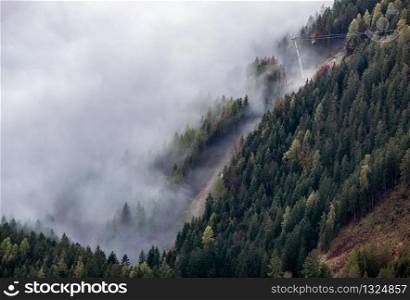 Cable car gondolas moving across the Alps mountain hill from misty cloud to the top. Autumn misty morning view. Picturesque traveling, seasonal, cloudy and misty weather condition background scene.