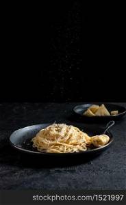 Cacio e Pepe - Italian Pasta with Cheese and Pepper on Black Plate on Dark Background.. Cacio e Pepe - Italian Pasta with Cheese and Pepper on Black Plate on Dark Background