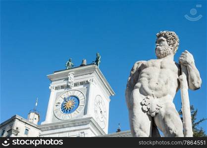 Caco statue with the background, the clock tower of the church. At Liberty Square, Udine Italy