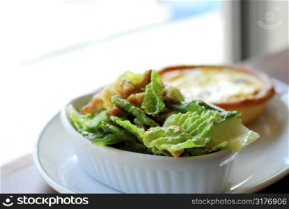 Caesar salad and quiche on white plate