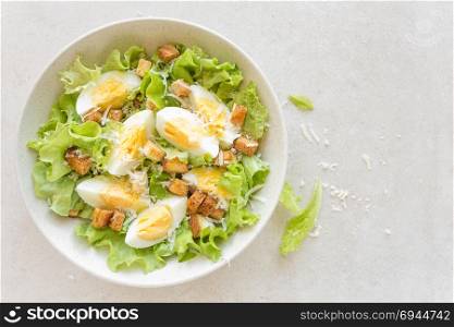 Caesar salad with eggs, lettuce and parmesan cheese on plate. Top view
