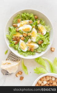 Caesar salad with eggs, lettuce and parmesan cheese on plate. Top view