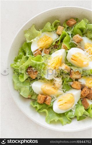 Caesar salad with eggs, lettuce and parmesan cheese on plate. Top view